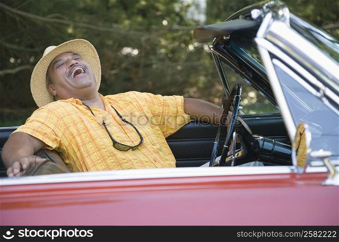 Senior man sitting in a convertible car and laughing