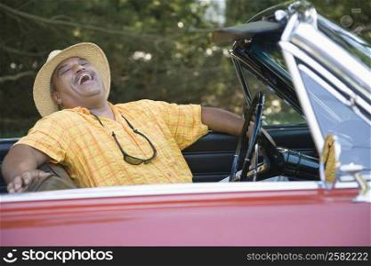 Senior man sitting in a convertible car and laughing