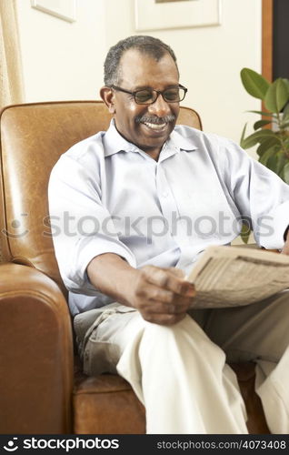 Senior Man Sitting In Armchair Reading Newspaper