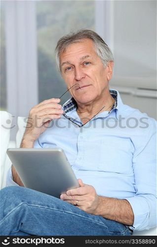 Senior man sitting in sofa with electronic tablet