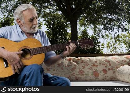 Senior man sitting on a couch and playing a guitar