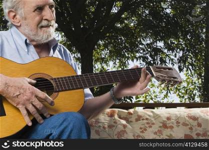 Senior man sitting on a couch and playing a guitar