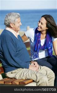 Senior Man Sitting On Bench With Adult Daughter By Sea