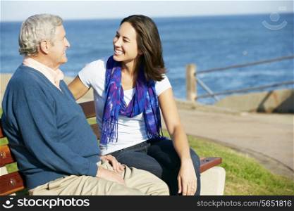 Senior Man Sitting On Bench With Adult Daughter By Sea
