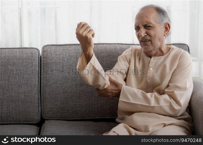 Senior man sitting on couch having pain in his arm.  Health and fitness  