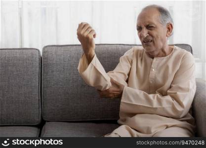 Senior man sitting on couch having pain in his arm.  Health and fitness  