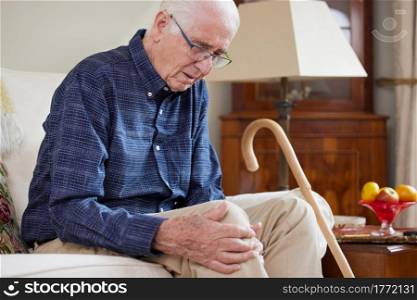 Senior Man Sitting On Sofa At Home Suffering With Knee Pain From Arthritis