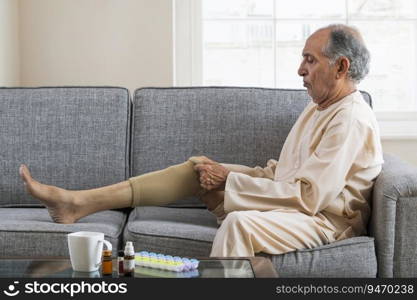 Senior man sitting on sofa putting on leg warmers.  Health and fitness  