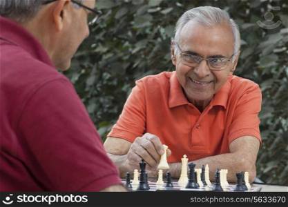 Senior man smiling at friend while holding chess piece