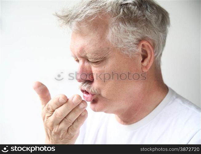 Senior man sneezes into his hand.