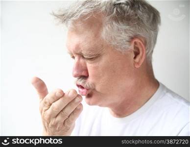 Senior man sneezes into his hand.