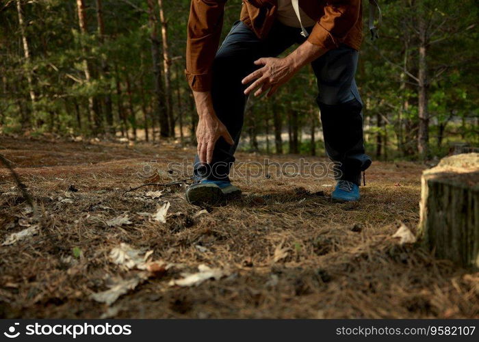 Senior man sprained leg during hiking trip outdoors in forest. Retired male traveler suffering from foot sore having health problem while walking footpath on nature. Senior man sprained leg during hiking trip outdoors in forest