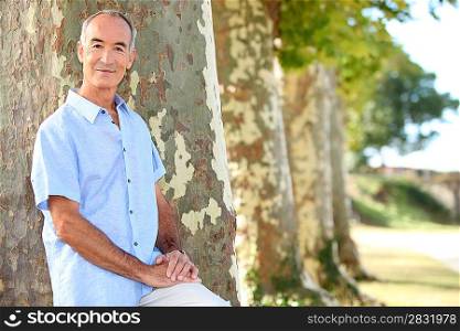Senior man standing by a row of trees