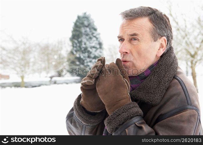 Senior Man Standing Outside In Snowy Landscape Warming Hands