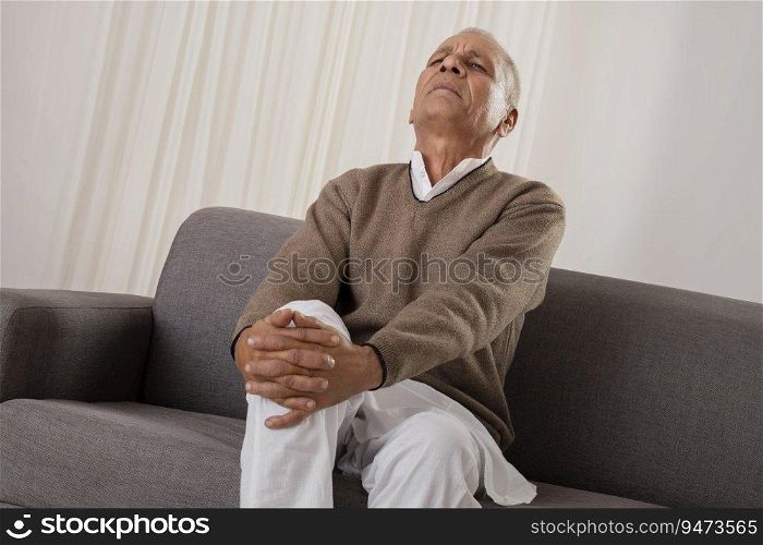 Senior man suffering from knee pain while sitting on sofa