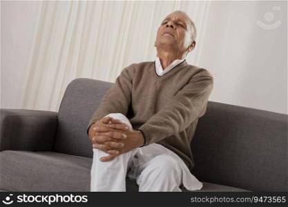 Senior man suffering from knee pain while sitting on sofa