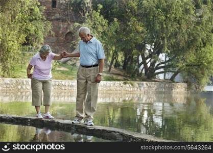 Senior man supporting woman while walking on narrow bridge at park