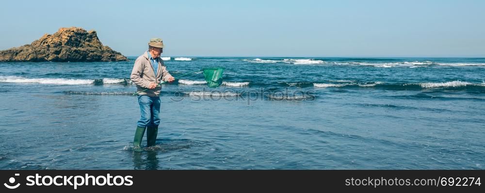 Senior man taking garbage out of the sea with a fishing net. Volunteer taking garbage out of the sea