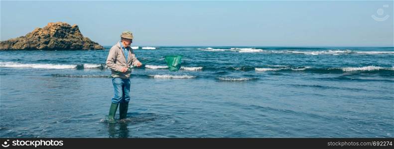 Senior man taking garbage out of the sea with a fishing net. Volunteer taking garbage out of the sea