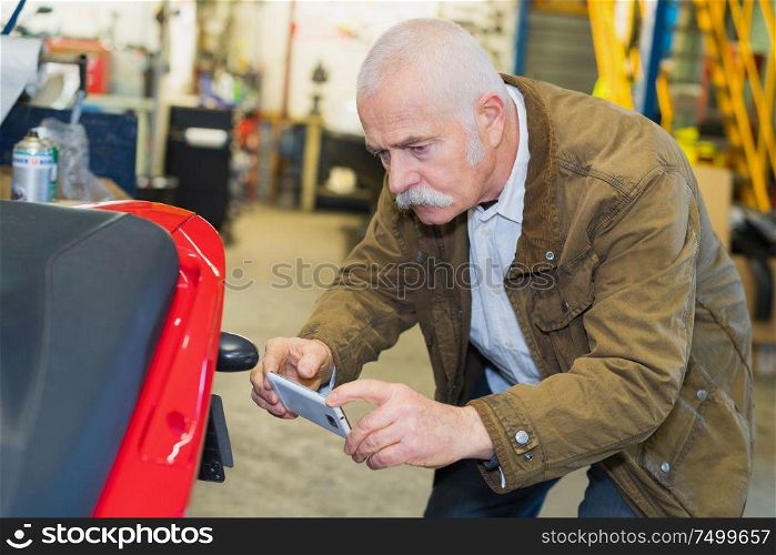 senior man taking photo of motorcycle plate in garage