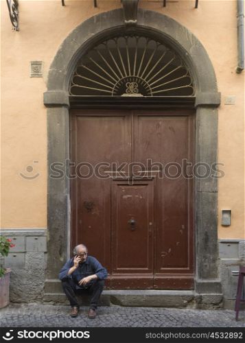 Senior man talking on mobile phone in front of doorway, Orvieto, Terni Province, Umbria, Italy