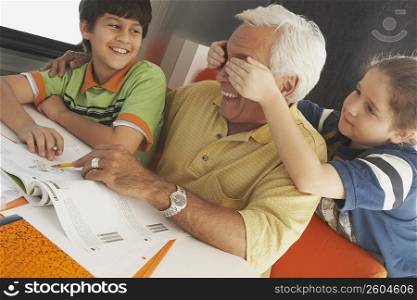Senior man teaching his grandson and her granddaughter covering his eyes with her hands from behind