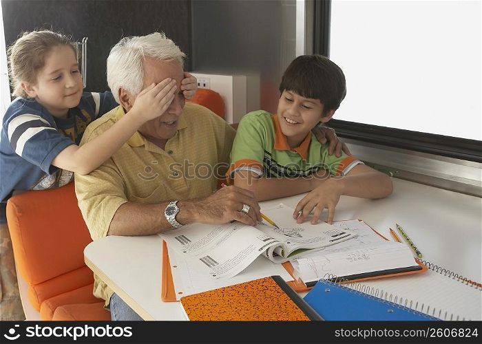 Senior man teaching his grandson and her granddaughter covering his eyes with her hands from behind