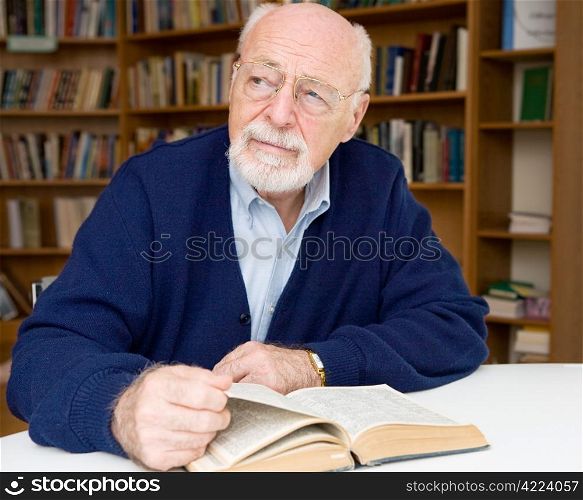 Senior man thinking about the book he is reading in the library.