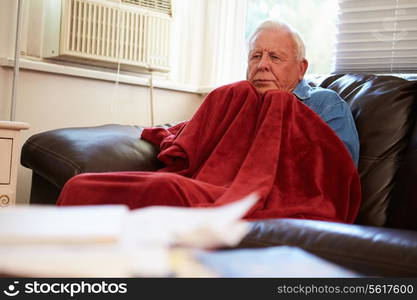 Senior Man Trying To Keep Warm Under Blanket At Home