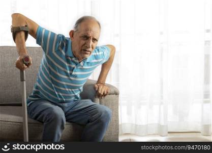 Senior man trying to stand up from couch with a Walking stick, Cane. (Health and fitness)  