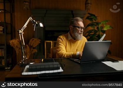 Senior man typing on laptop keyboard while sitting at table and working at home office in evening. Senior man typing on laptop keyboard working at home office