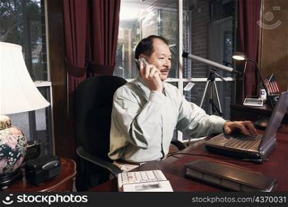 Senior man using a laptop talking on a cordless telephone