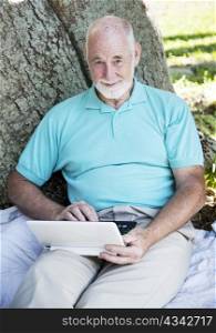 Senior man using a netbook computer outdoors under a tree.