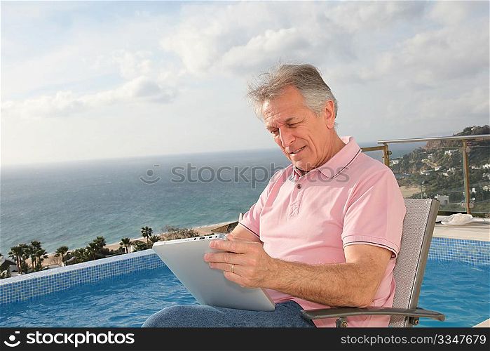 Senior man using electronic tablet by a swimming-pool
