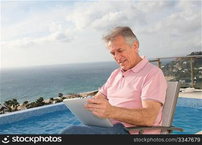 Senior man using electronic tablet by a swimming-pool