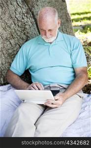 Senior man using his wireless netbook computer outdoors.