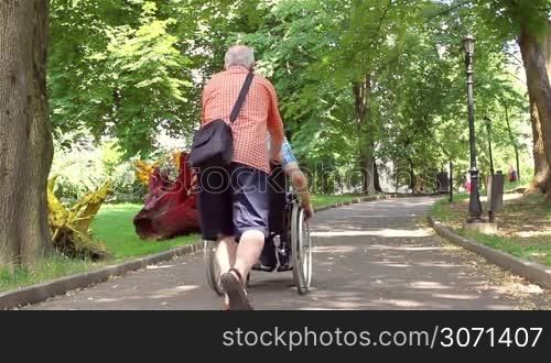 Senior man walking with disabled young man in wheelchair in the park.
