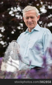 Senior Man Watering Flowers In Garden With Hose