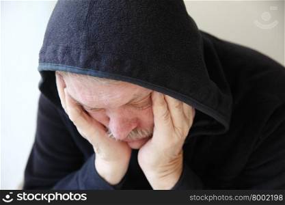 Senior man wearing a dark hoodie slumps in depression .