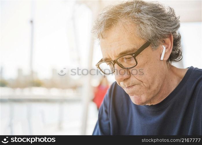 senior man wearing eyeglasses with white bluetooth earphone his ear