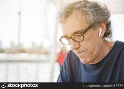 senior man wearing eyeglasses with white bluetooth earphone his ear