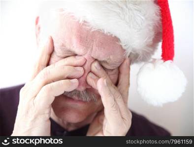 senior man wearing holiday hat has pain in his sinus area