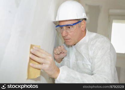senior man wearing protection sanding interior wall for restoration