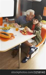 Senior man whispering into his grandson&acute;s ear at the dining table