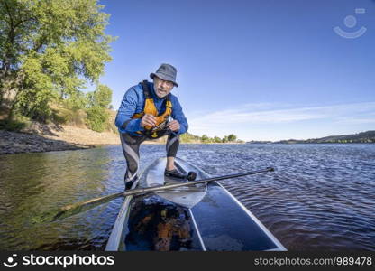 senior man with a stand up paddleboard on a shore of a mountain lake - Horsetooth Reservoir , COlorado, in early fall scenery