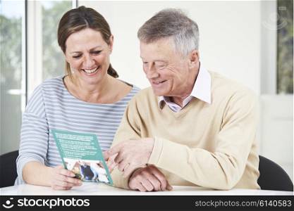 Senior Man With Adult Daughter Looking At Brochure For Retirement Home
