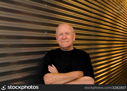 Senior man with arms folded in front of steel background.