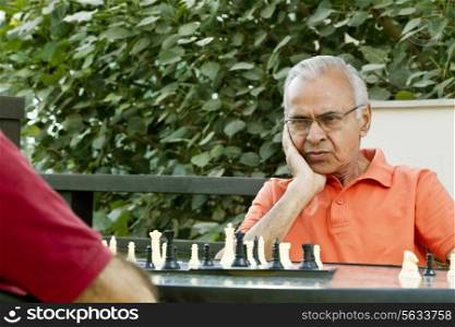 Senior man with hand on chin looking at chess board and thinking of his next move