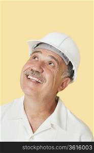 Senior man with hardhat looking up and smiling over yellow background