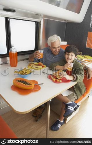 Senior man with his grandson drinking juice and smiling at the dining table